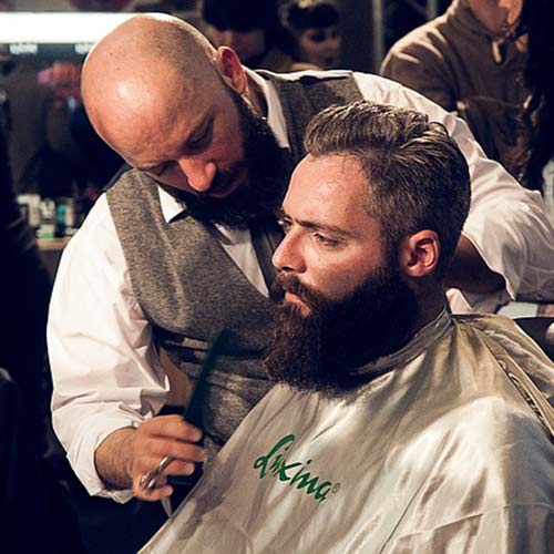 Un homme taille la barbe d'un client dans un salon de barbiers. Au Québec, le mot barbier signifie aussi salon de coiffure pour hommes.